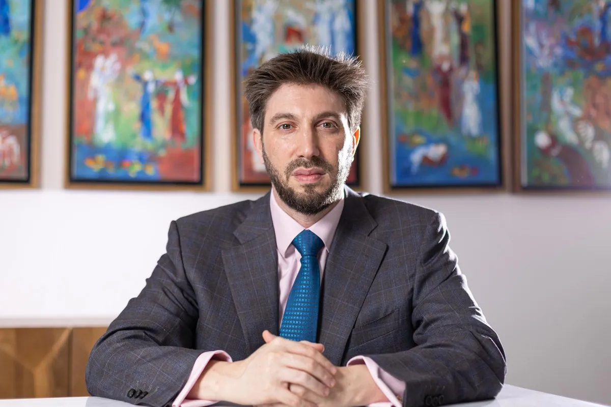 Daniel Seal seated at a table in front of colourful paintings